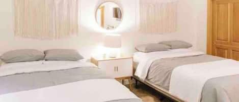 Een slaapkamer met twee bedden, een nachtkastje, een spiegel en een houten deur.