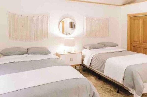 A bedroom with two beds, a nightstand, a mirror, and a wooden door.