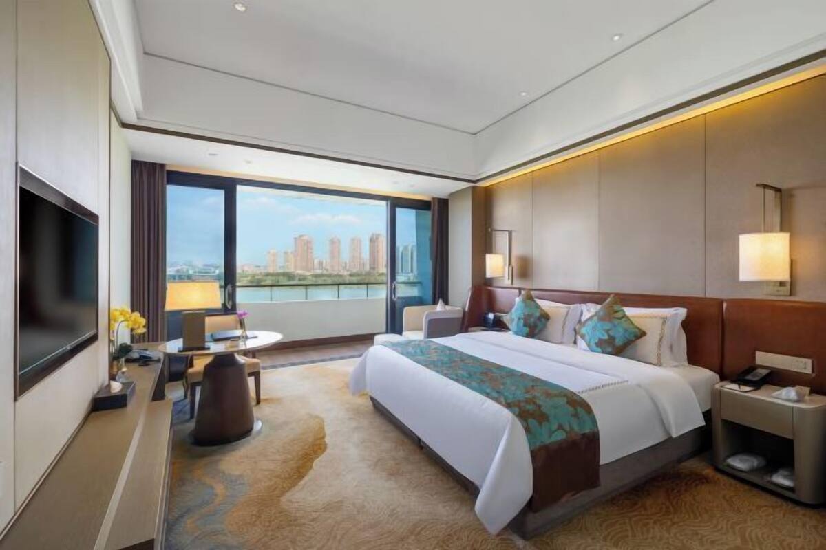 Ein Hotelzimmer mit einem großen Bett, einem Schreibtisch, einem Stuhl, einem Fernseher und Blick auf die Stadt.