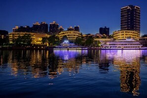 A waterfront hotel with a reflection in the water, featuring a large building with multiple balconies and a boat docked nearby.