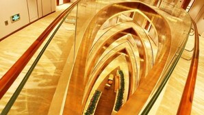 Een modern hotelinterieur met een centrale glazen liftput en een gebogen, metalen structuur.