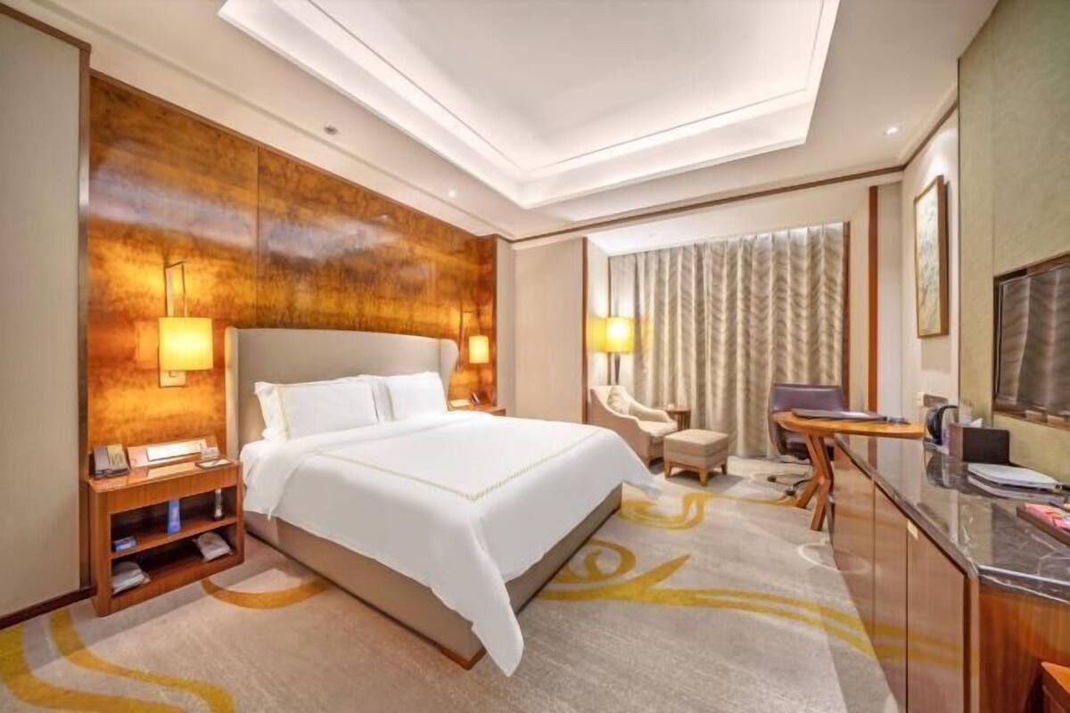 Ein Hotelzimmer mit einem großen Bett, einem Schreibtisch, einem Stuhl, einem Nachttisch und einer Lampe.