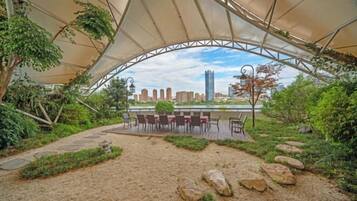 An outdoor seating area with a canopy, stone pathway, and a view of a city skyline.