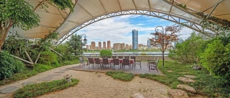 An outdoor seating area with a canopy, stone pathway, and a view of a city skyline.