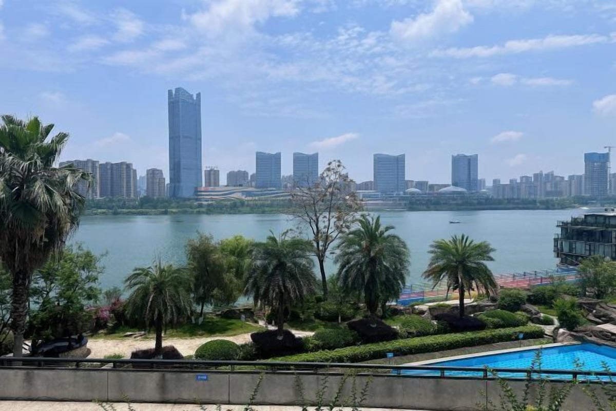 Une vue urbaine comprenant un gratte-ciel imposant, une étendue d’eau et un espace piscine agrémenté de palmiers.