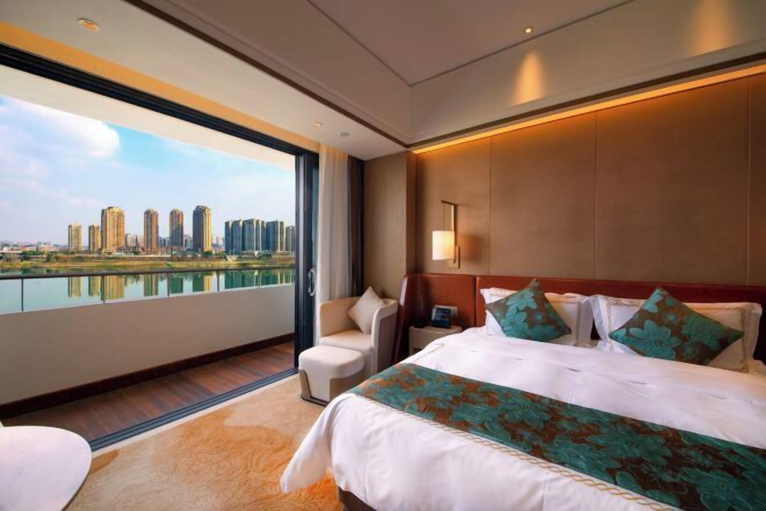 A modern hotel room with a large bed, a desk, and a view of a city skyline.