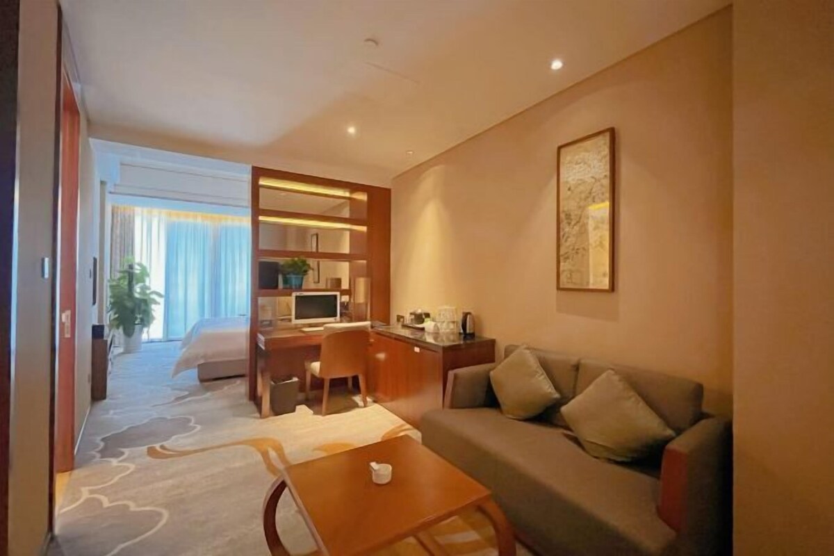Une chambre d’hôtel avec un canapé, une petite table, un bureau avec une chaise, un lit et une grande fenêtre avec des rideaux.