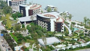 Een modern hotel met een golvend ontwerp, meerdere balkons en een aangelegde tuin met een zwembad.
