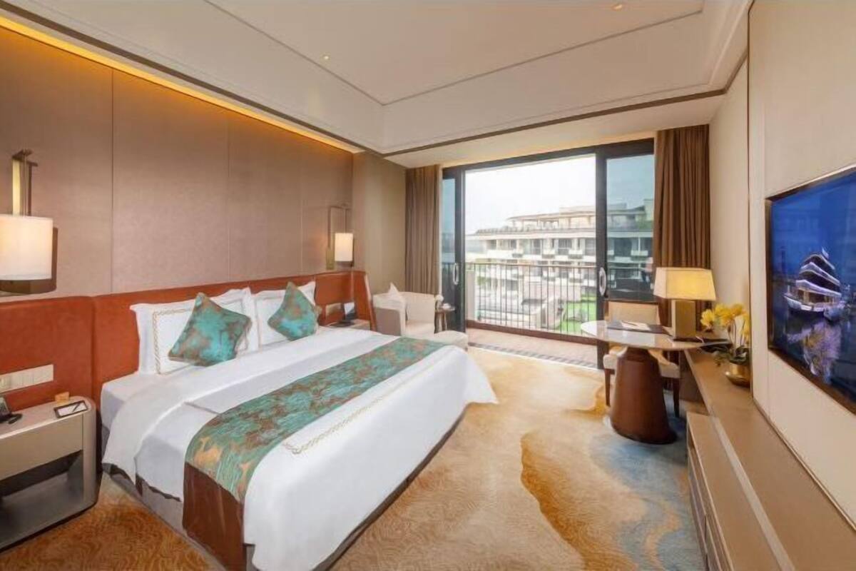 Ein Hotelzimmer mit einem großen Bett, einem Schreibtisch, einem Fernseher und einem Balkon mit Blick auf die Stadt.