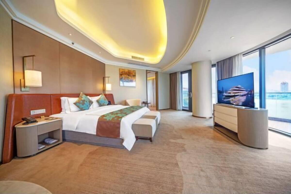 Ein Hotelzimmer mit einem großen Bett, einem Fernseher, einem Schreibtisch und Blick auf die Stadt.