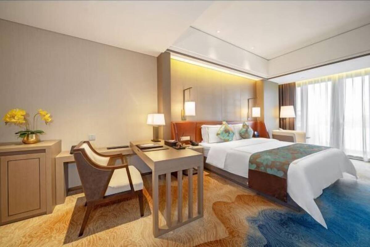 Ein Hotelzimmer mit Bett, Schreibtisch, Stuhl, Nachttischlampen und einem Fenster mit Vorhängen.