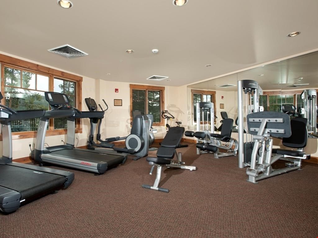 Une salle de sport équipée de tapis de course, d’appareils de musculation et d’un mur entièrement recouvert de miroirs.