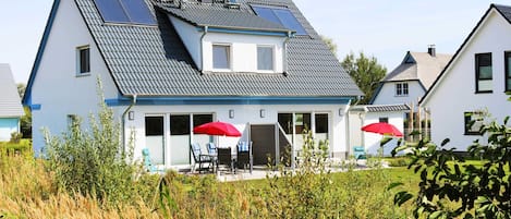 A two-story house with a sloped roof, solar panels, and a covered patio with red umbrellas.