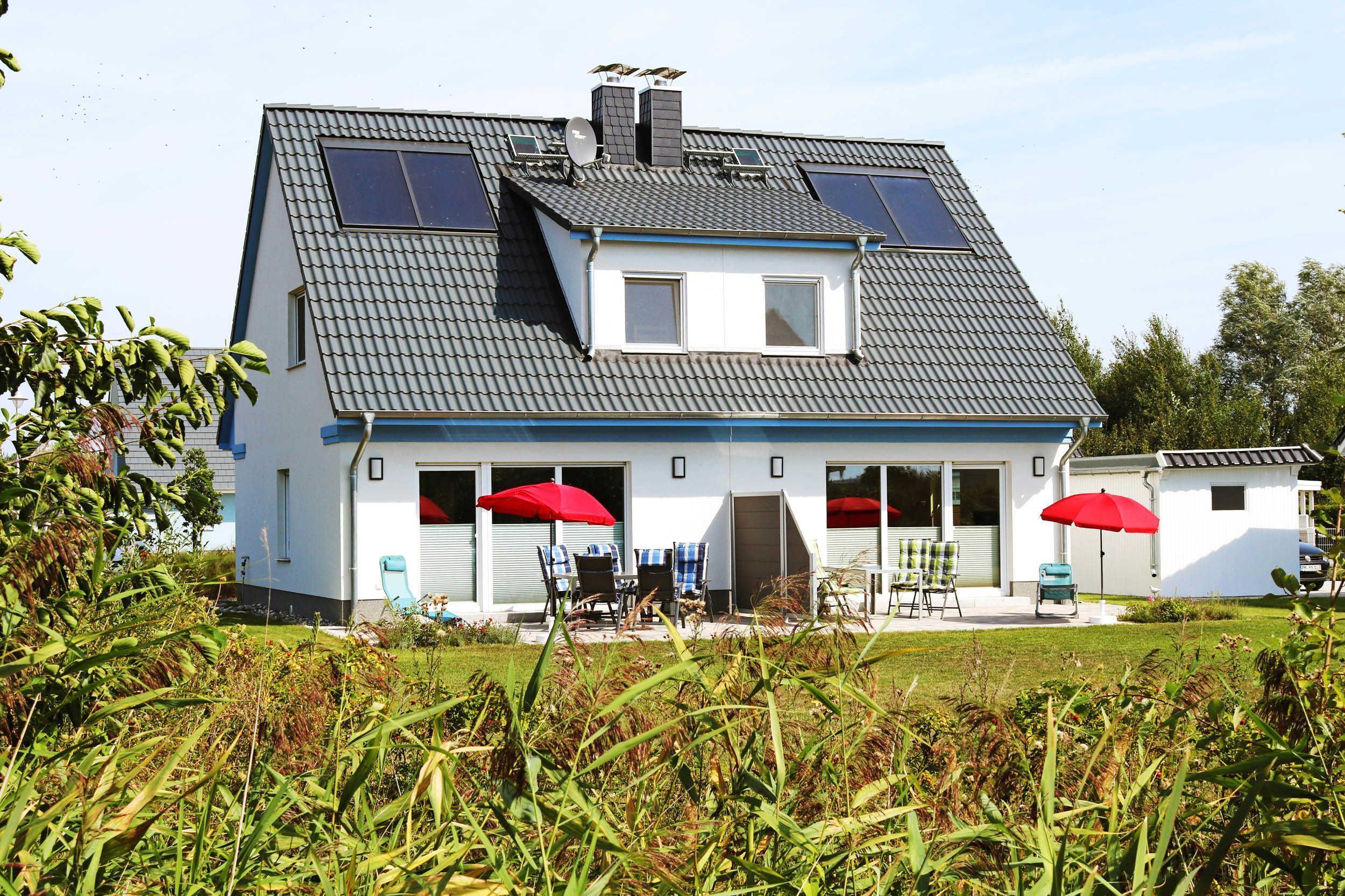 Ein zweistöckiges Haus mit Satteldach, Solaranlage und einer Veranda mit roten Sonnenschirmen.