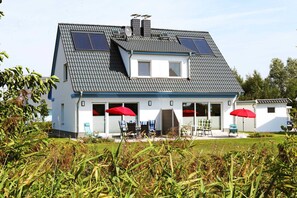 A two-story house with a sloped roof, solar panels, and a covered patio with outdoor furniture.