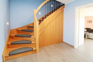 A wooden staircase with a curved design and a glass railing, leading to a room with a light blue wall and a wooden floor.