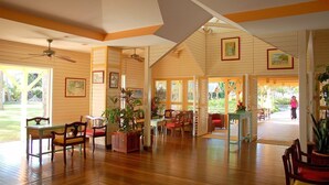 A spacious room with wooden floors, a dining area with chairs and a table, and a view of a garden through large windows. - CHARMING STUDIO with swimming pool in Martinique (les trois ilets)