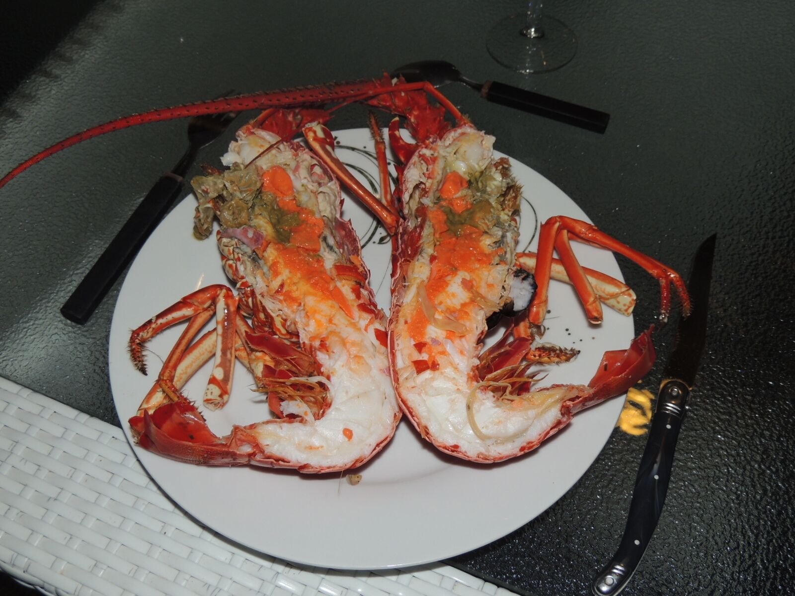A lobster on a white plate with a knife and fork beside it.
