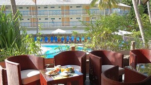 An outdoor seating area with wicker furniture, a pool, and a building with balconies in the background. - CHARMING STUDIO with swimming pool in Martinique (les trois ilets)
