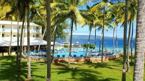 A resort with a pool area surrounded by palm trees, a building with balconies, and a view of the ocean. - CHARMING STUDIO with swimming pool in Martinique (les trois ilets)