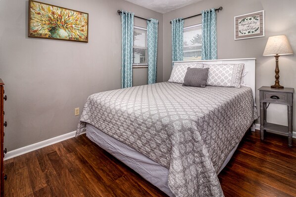 A bedroom with a bed, curtains, a lamp, and a painting on the wall.