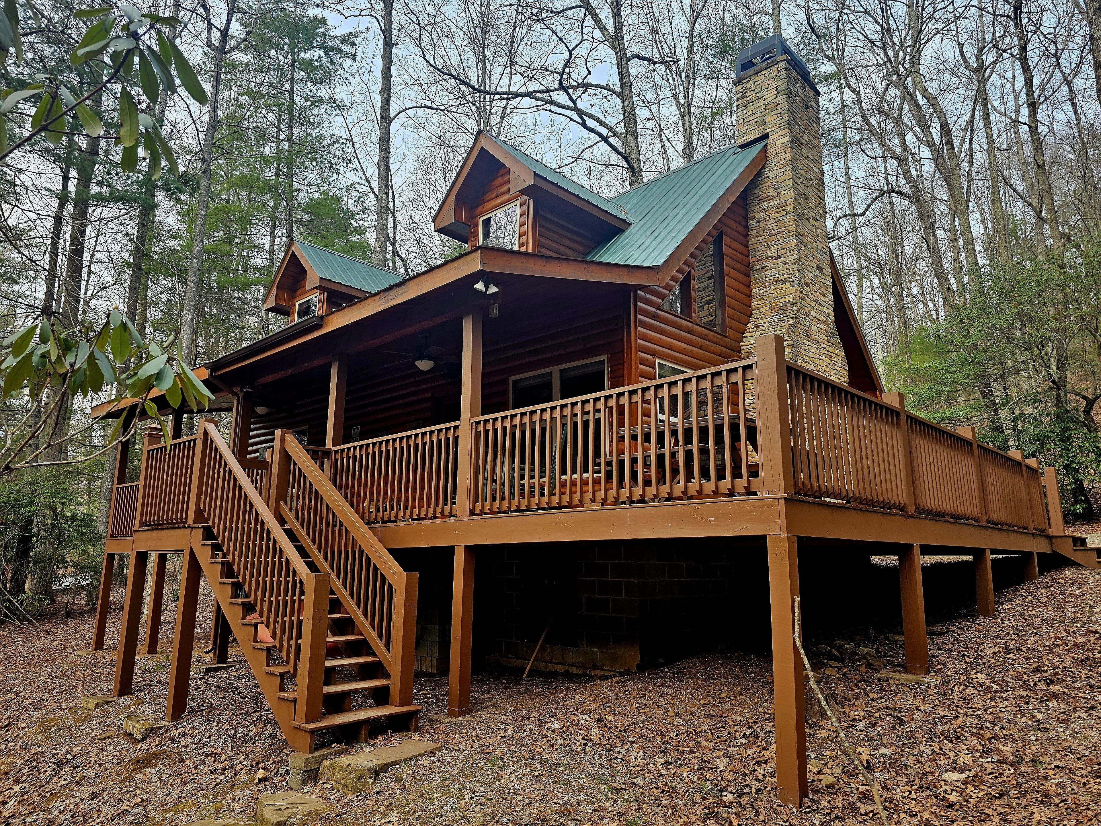 A cabin with a wooden deck, a staircase, and a chimney.
