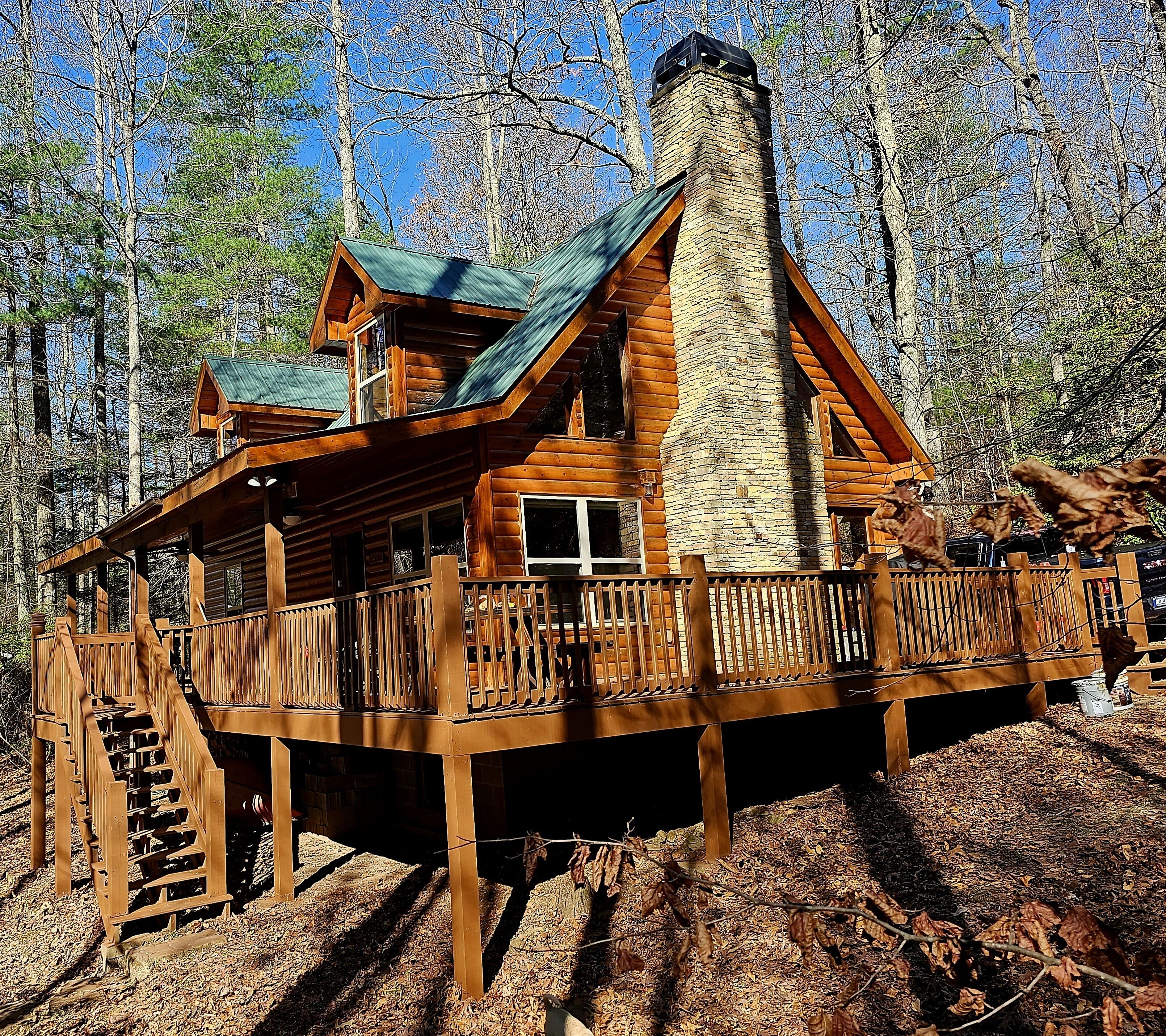 A log cabin with a stone chimney, wooden deck, and a staircase leading to the entrance.