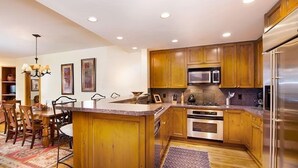 A modern kitchen with wooden cabinets, stainless steel appliances, and a dining area with a chandelier. - Elegant Condo in Beaver Creek (Edwards)