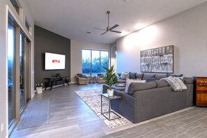 Un salon moderne avec un canapé gris, une table basse, un téléviseur fixé au mur et un ventilateur de plafond.