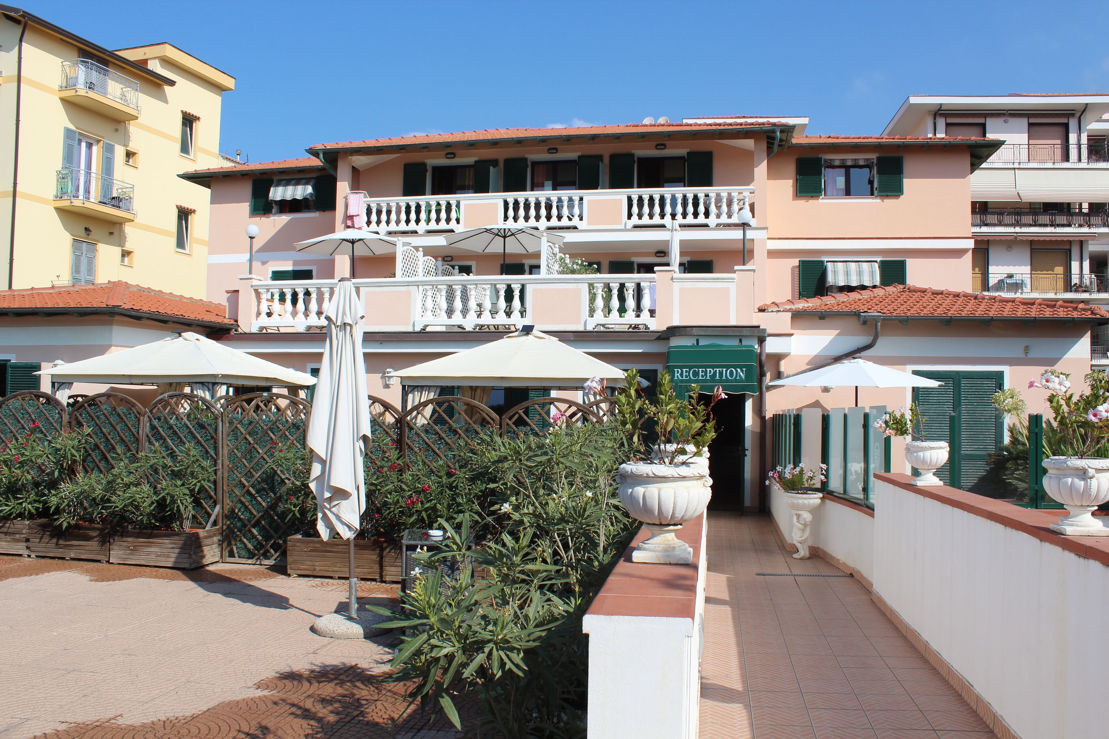 A hotel with a reception area, outdoor seating with umbrellas, and a garden with potted plants.