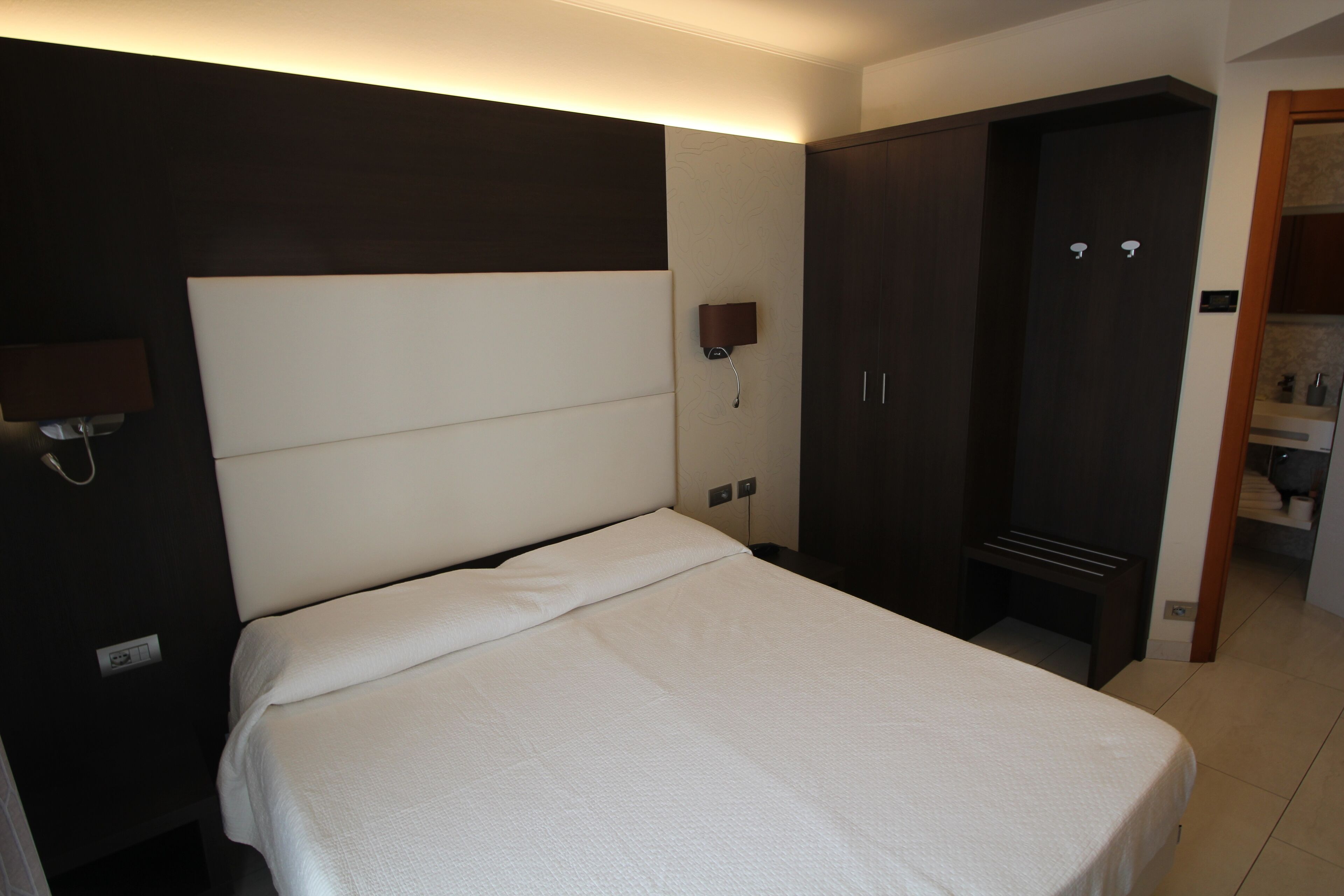 Una habitación de hotel con una cama, un armario y una lámpara fijada a la pared.
