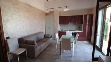 Una sala de estar moderna con un sofá, sillas, una mesa de comedor y una zona de cocina con armarios y un lavabo.