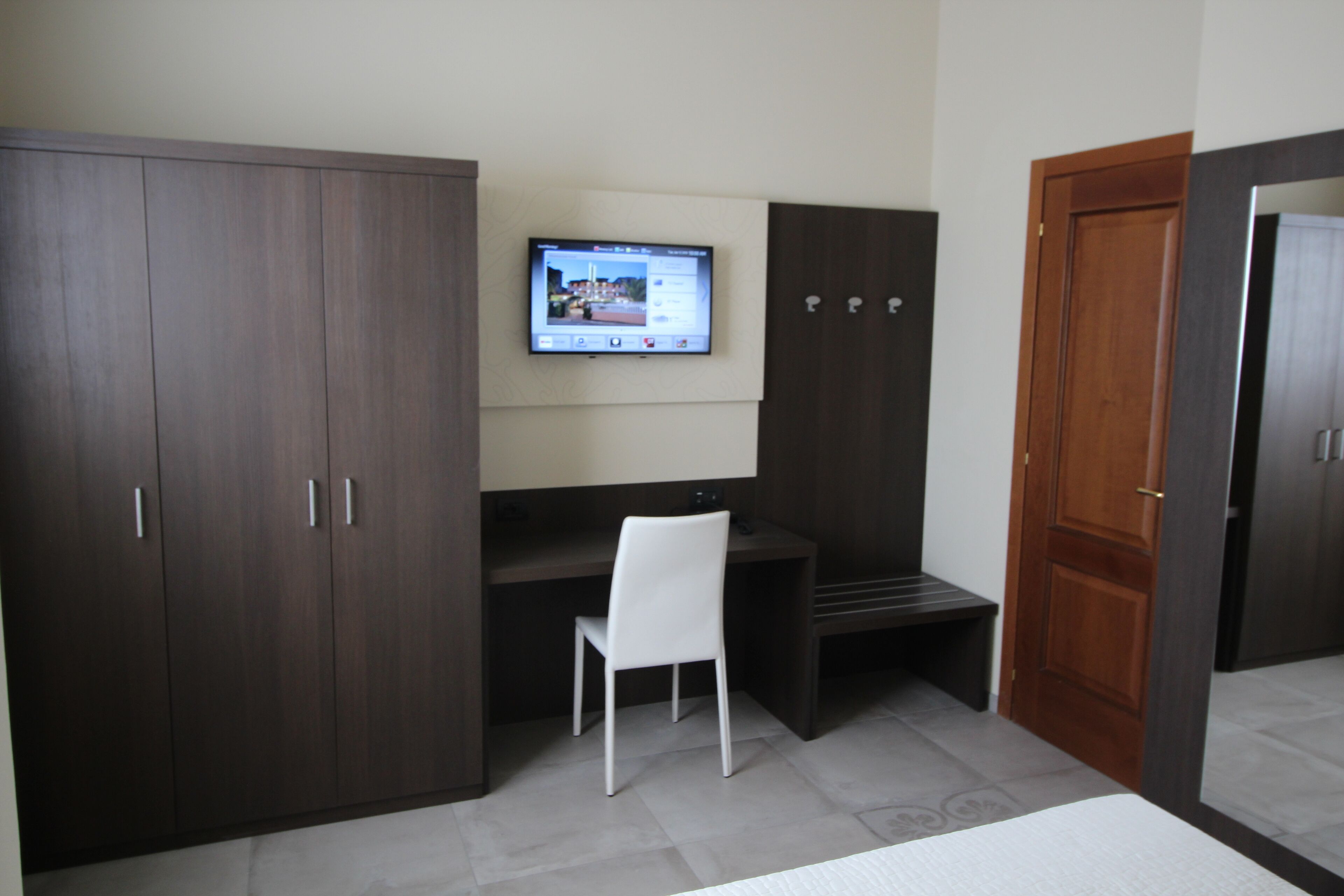 Una habitación con escritorio, silla, televisor montado en la pared y armario.