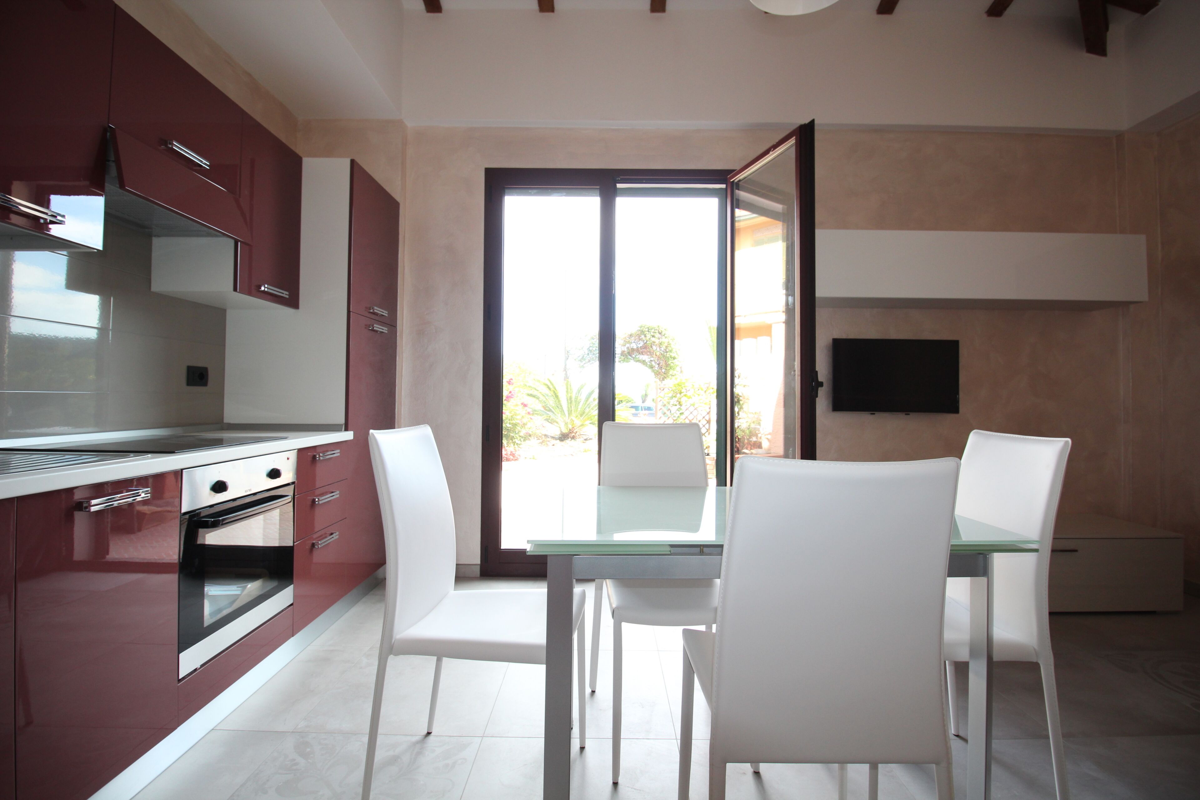 A modern kitchen with white chairs, a glass table, and a large window.