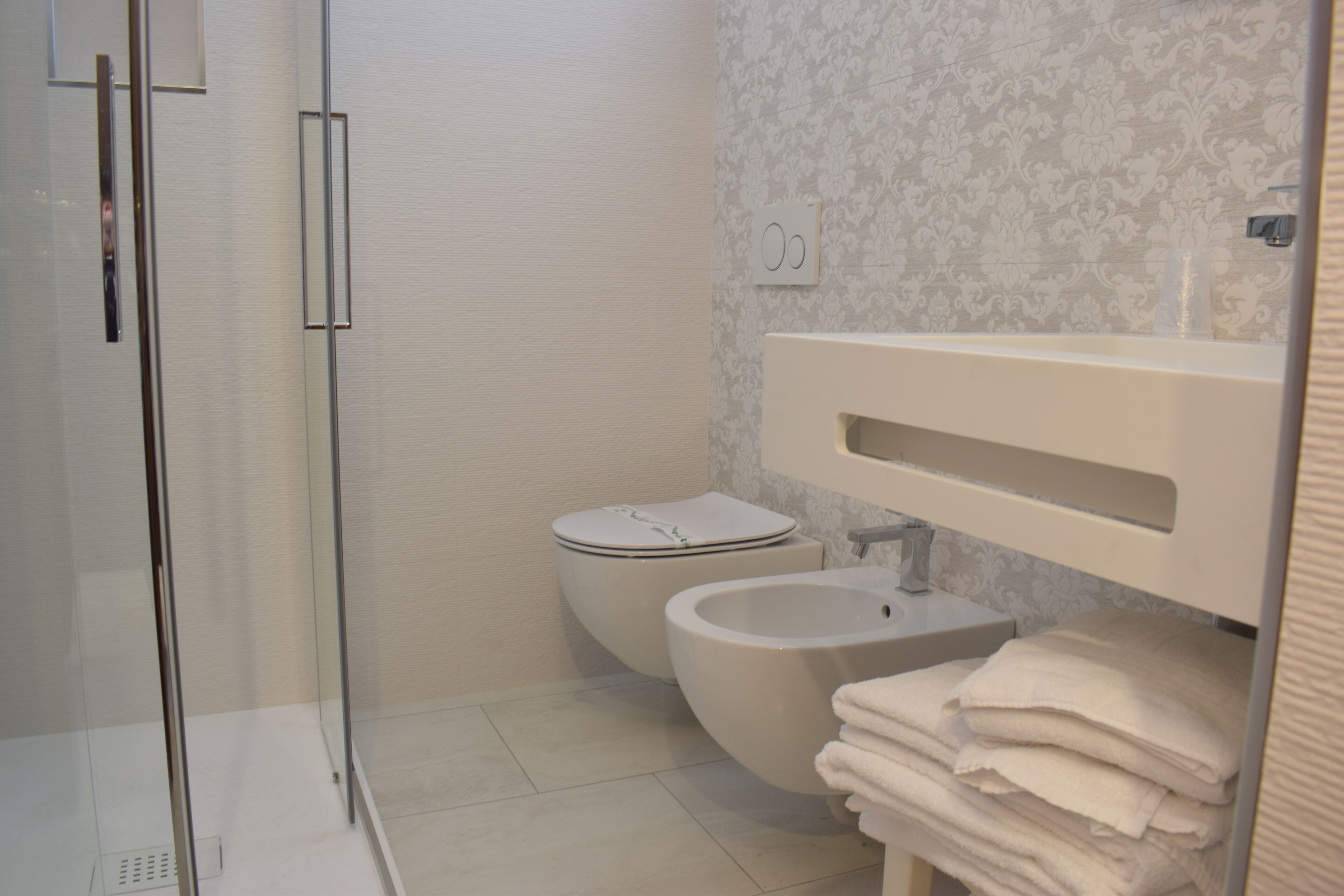 Une salle de bain avec une douche à parois de verre, des toilettes, un bidet et un lavabo avec des serviettes pliées.