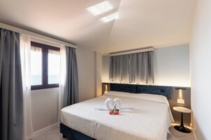 Quarto de hotel com cama, cortinas, mesa de cabeceira e criado-mudo.