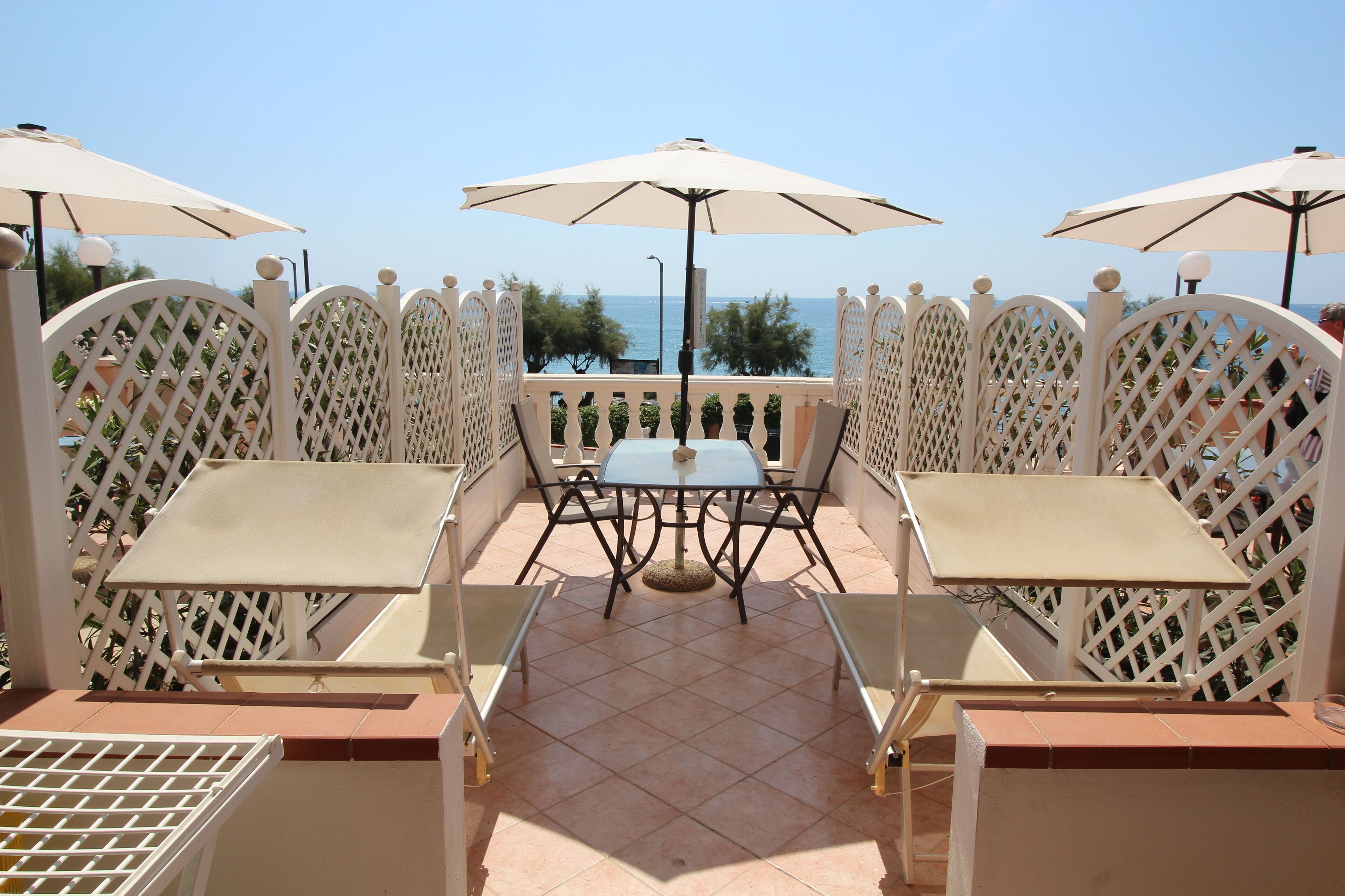An outdoor seating area with tables and chairs, surrounded by a white lattice fence, overlooking a body of water.