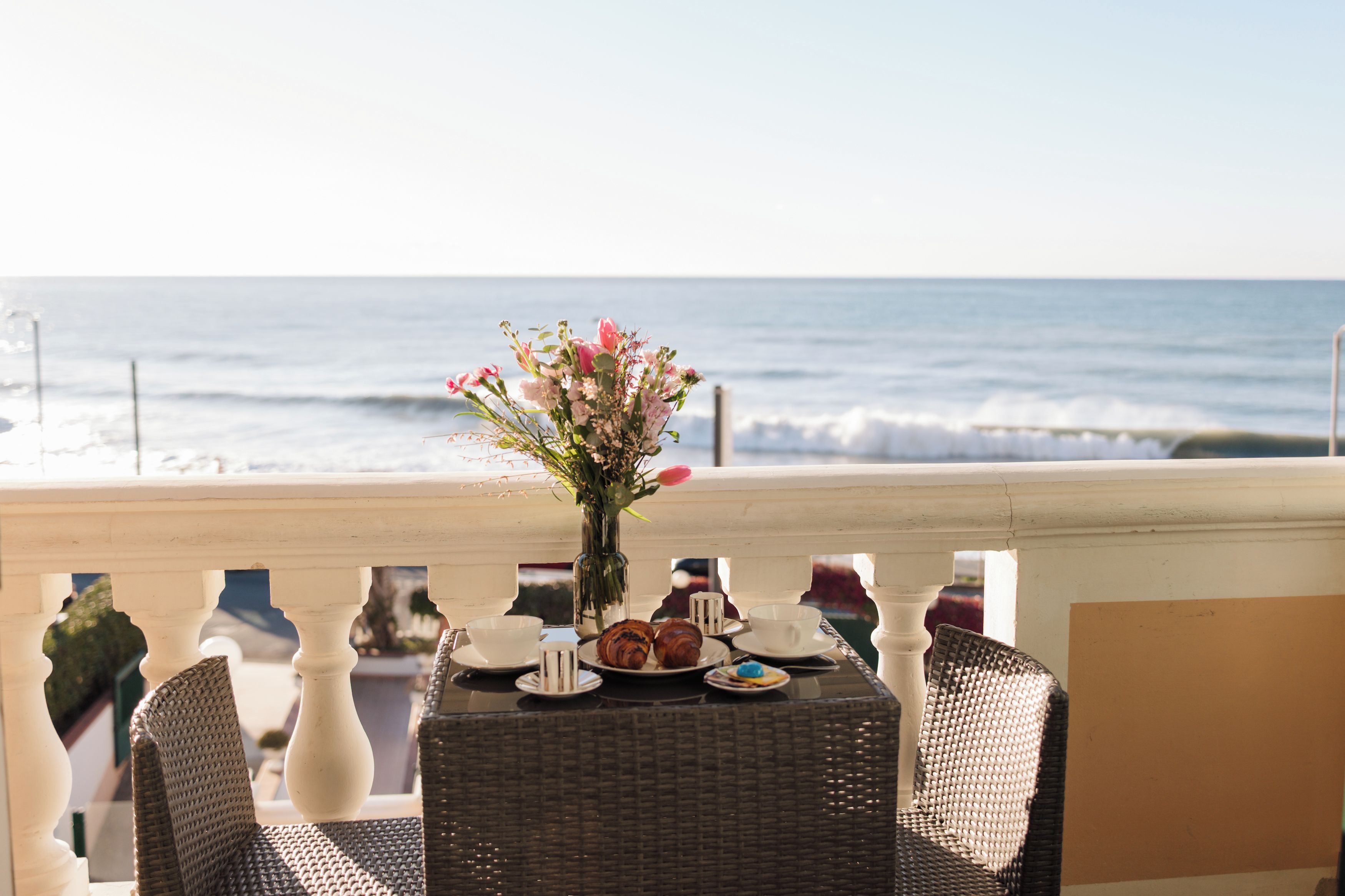 A table with a vase of flowers, plates with food, and a view of the ocean.