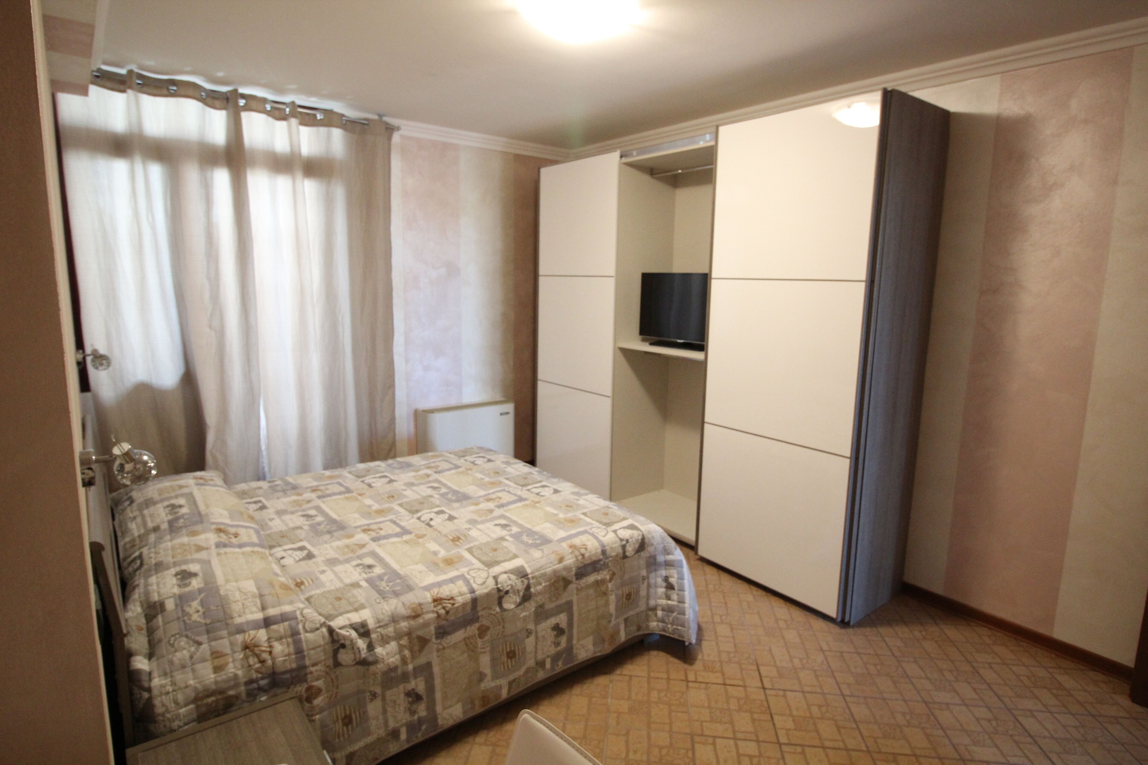 Un dormitorio con cama, armario y televisor en una estantería.