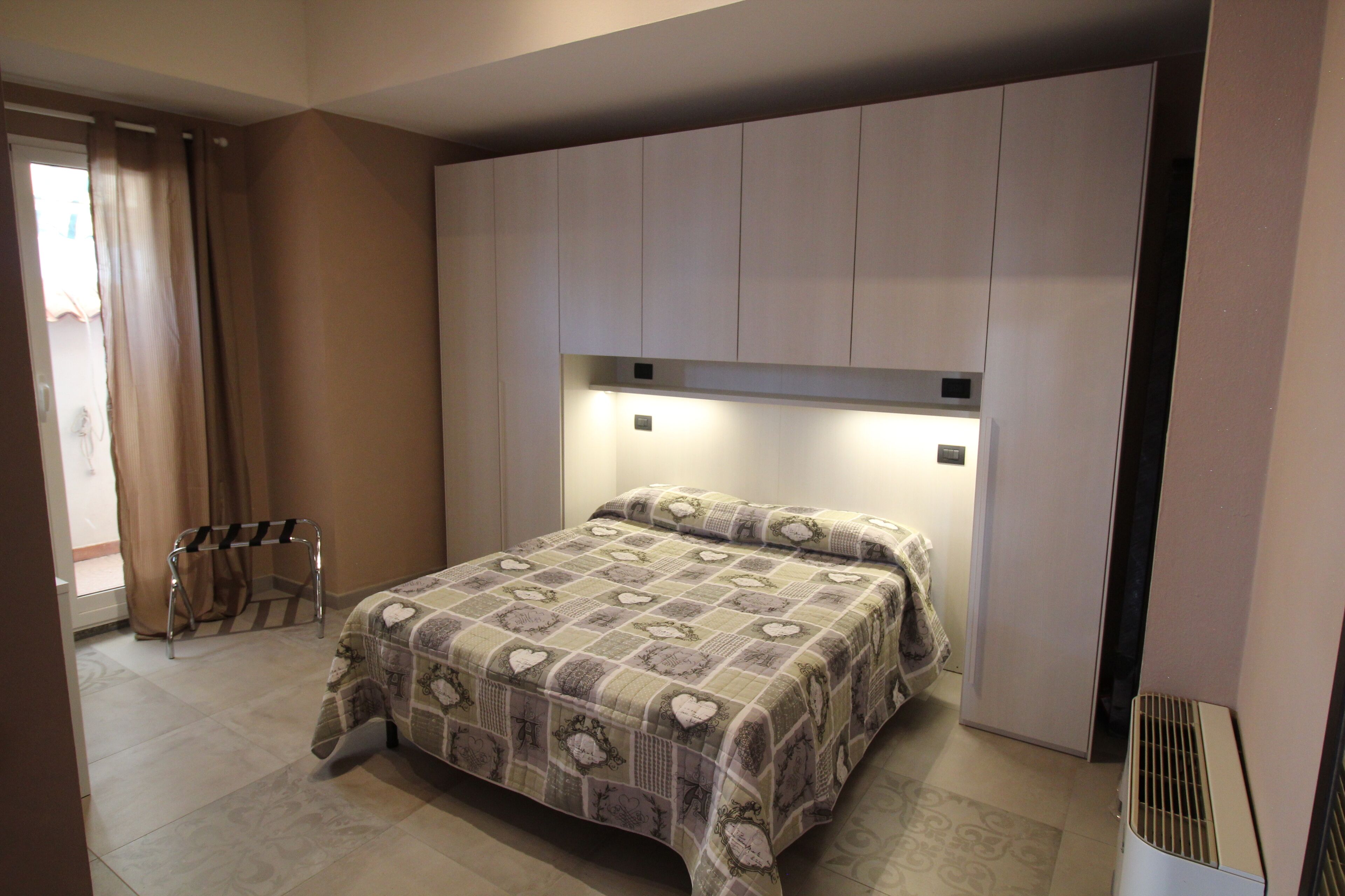 Una camera da letto con un letto, un armadio, un termosifone e una finestra con tende.