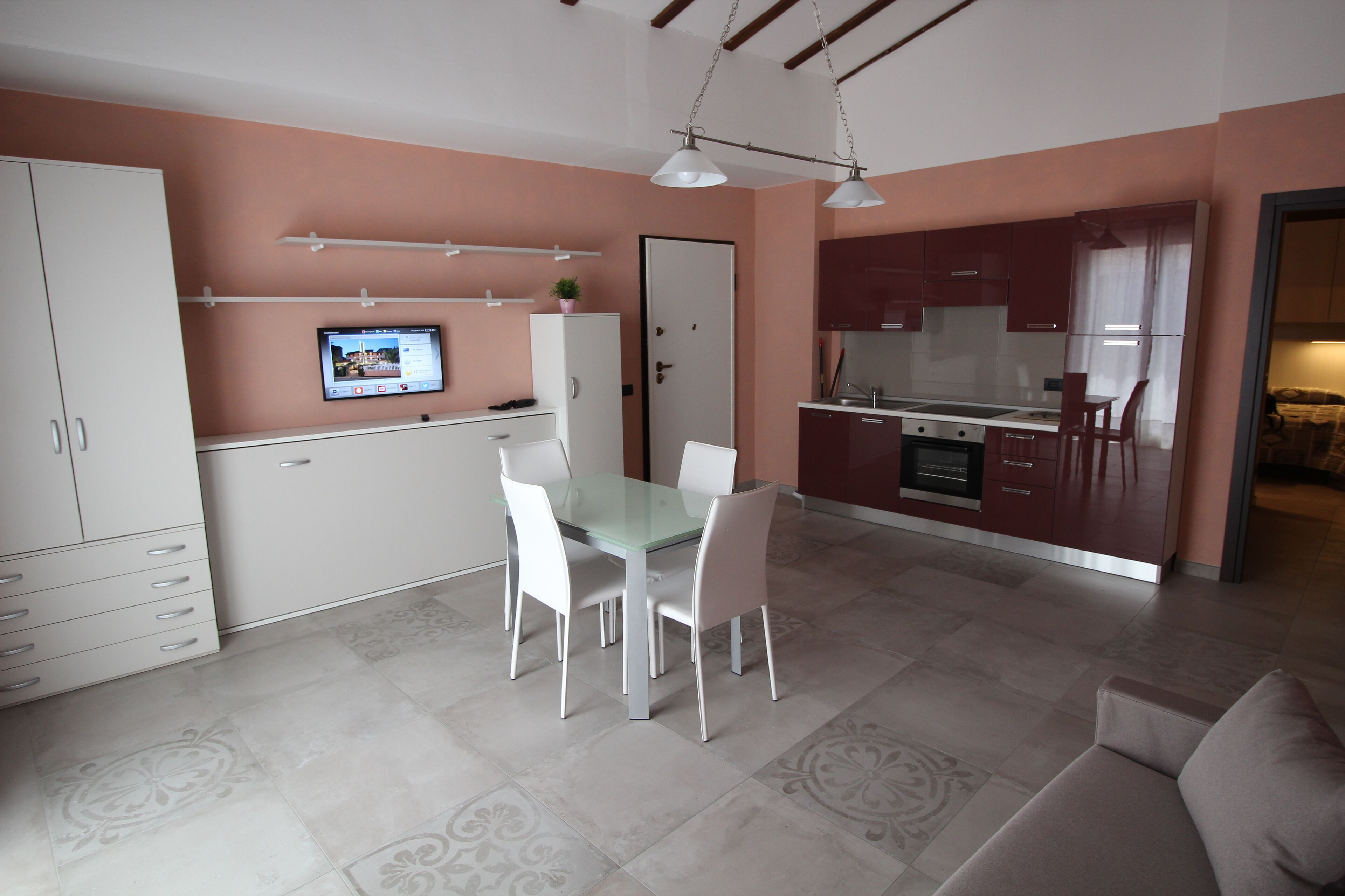 Una cocina compacta con comedor, armarios blancos, un televisor montado en la pared y un sofá en la sala.