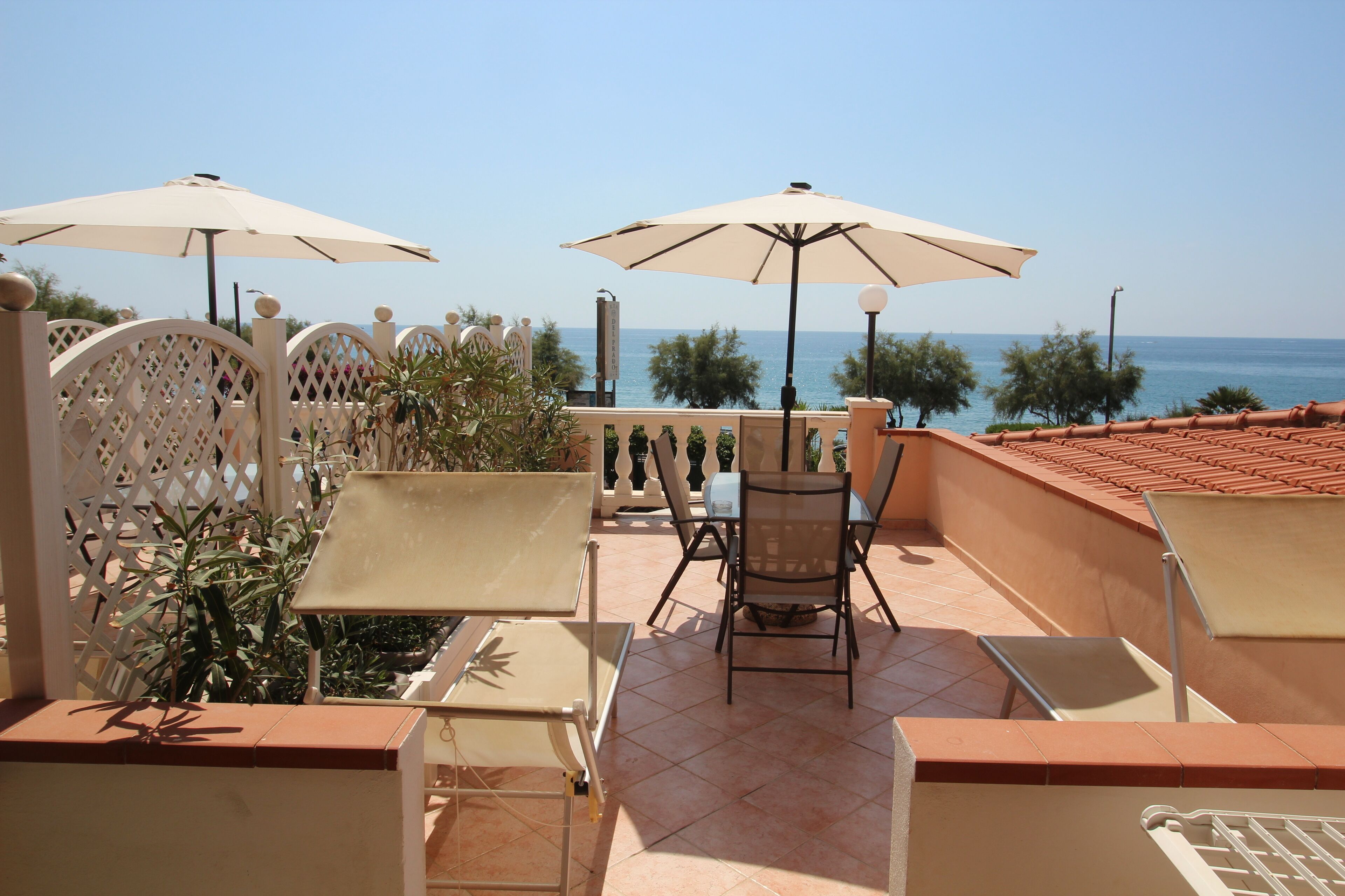 Une terrasse avec deux tables et des chaises, chacune agrémentée d’un parasol, donnant sur la mer.