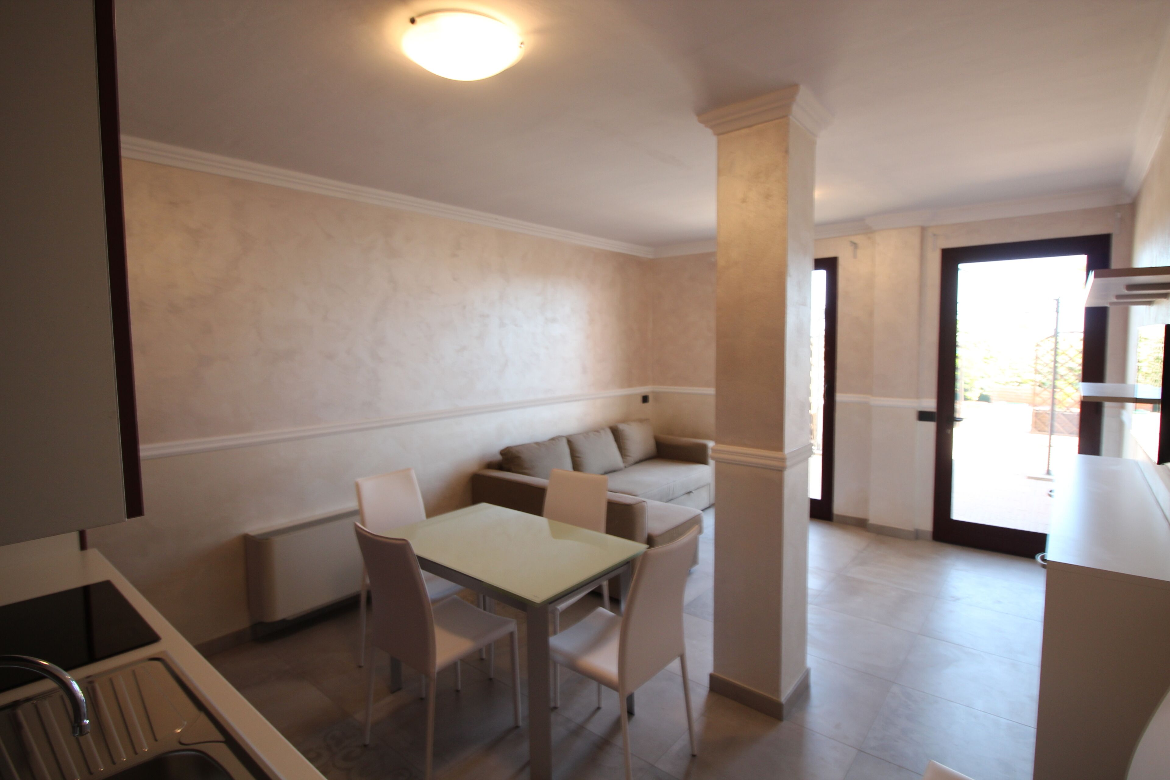 Una cocina compacta con comedor, un sofá y una puerta que da a un balcón.