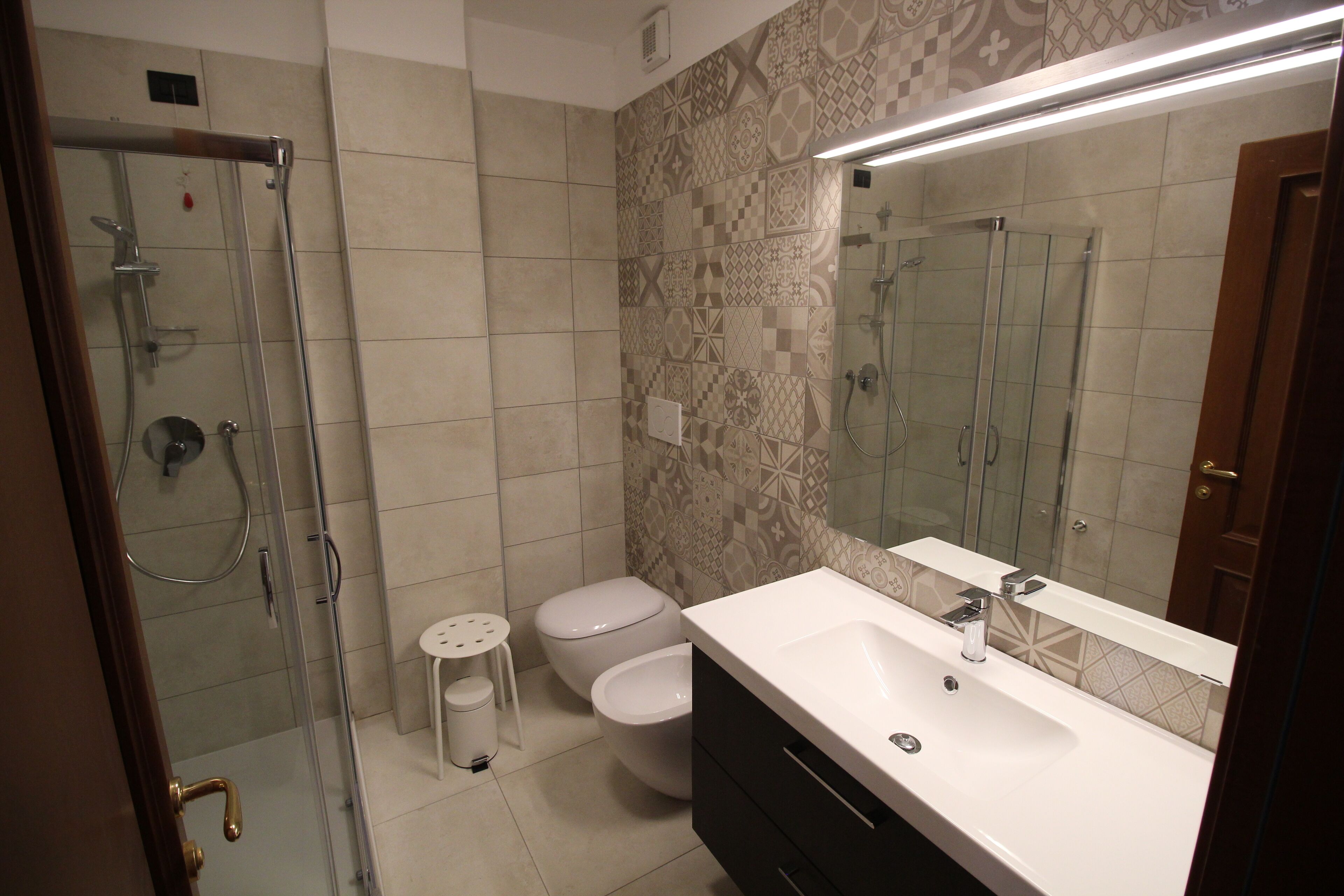 A bathroom with a glass-enclosed shower, two toilets, a sink, and a mirror.