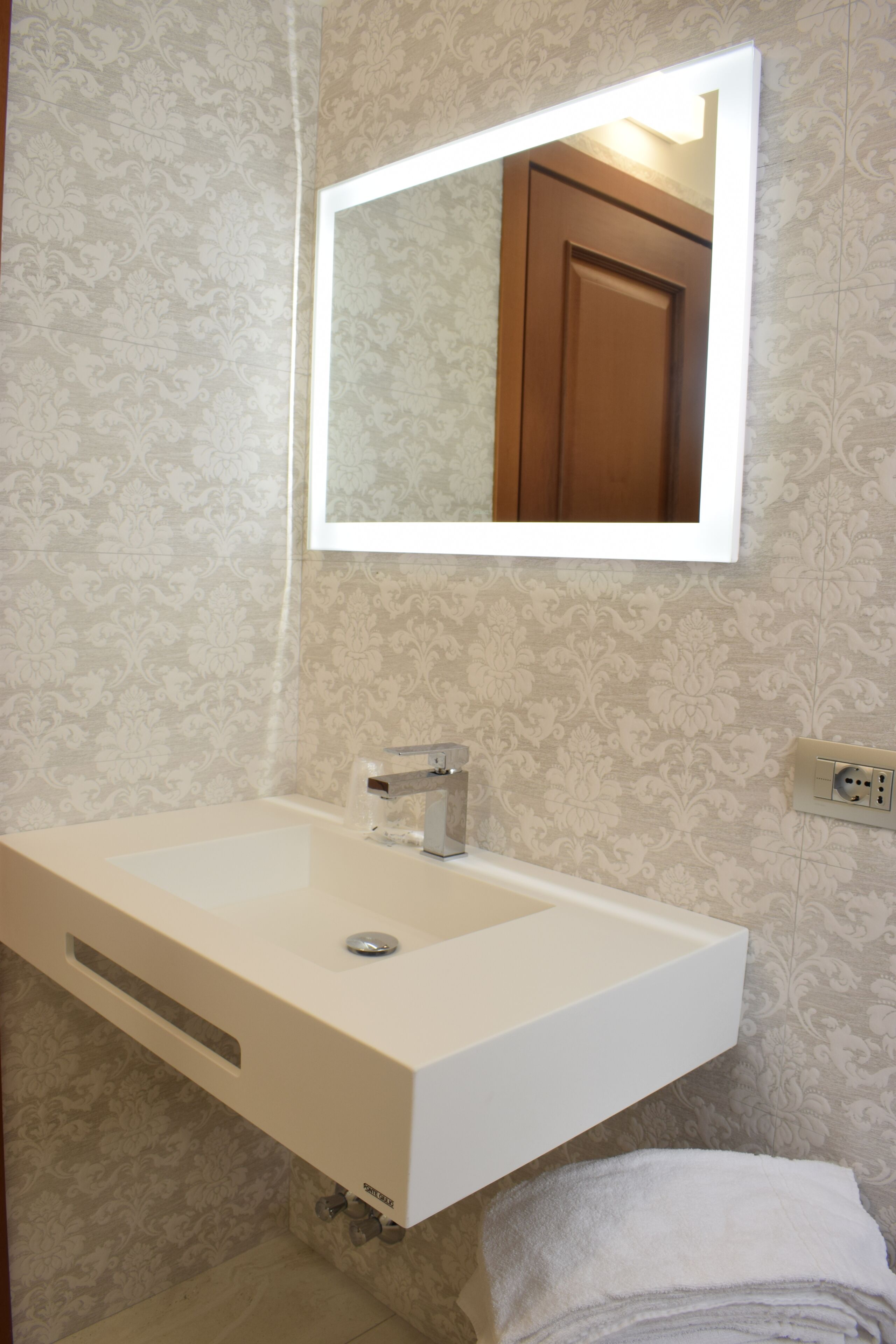Une salle de bain avec un lavabo blanc, un miroir au-dessus et une serviette sur le sol.