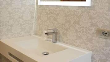 Une salle de bain avec un lavabo blanc, un miroir au-dessus et une serviette sur le sol.