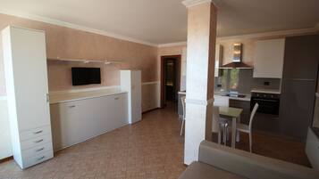 Cocina compacta con armarios blancos, horno empotrado y un televisor de pantalla plana sobre la encimera.