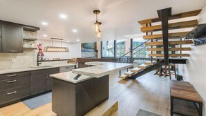 A modern kitchen with dark cabinetry, a central island, and a staircase with wooden steps.