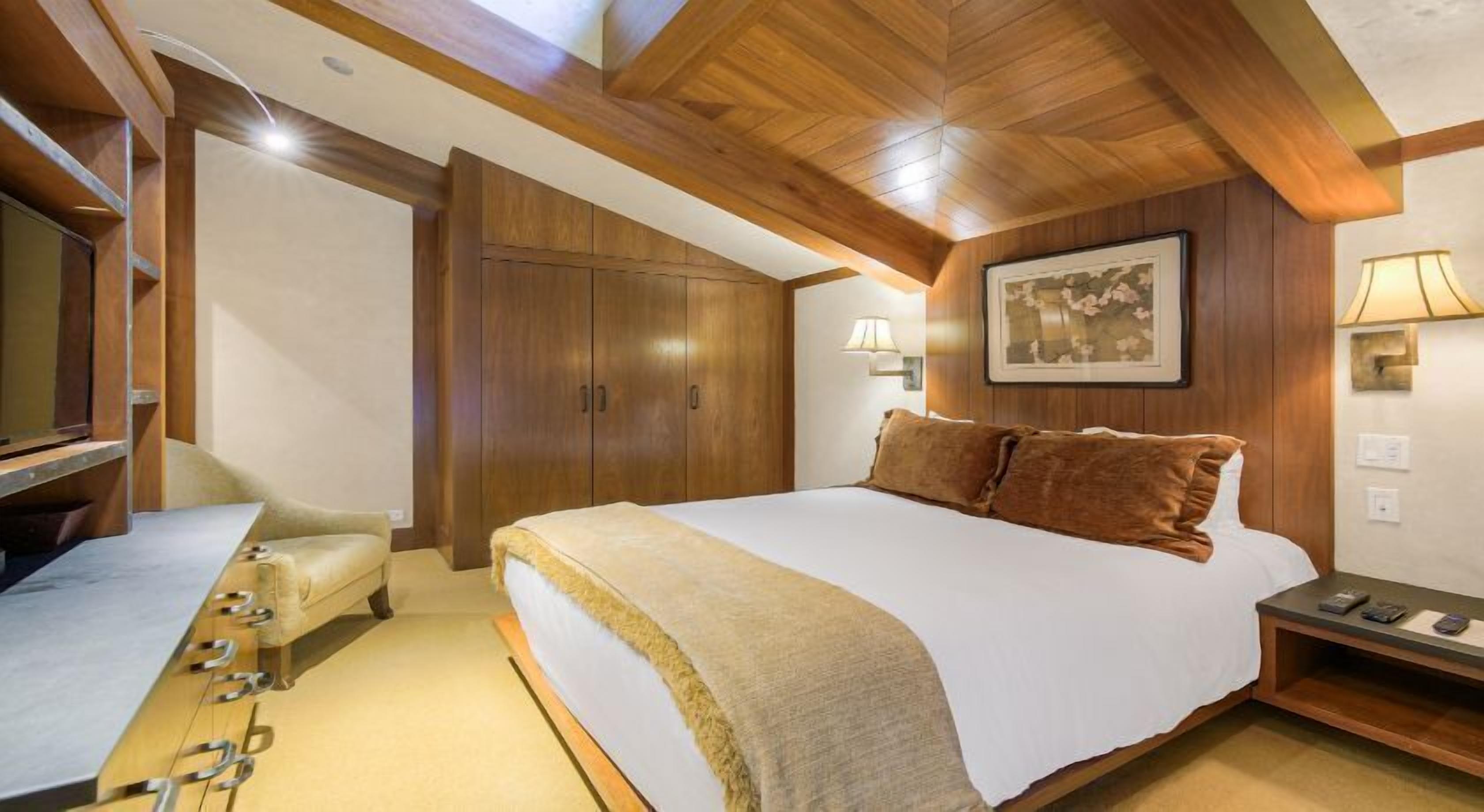 Une chambre à coucher avec un grand lit, un plafond en bois et un bureau avec une lampe.