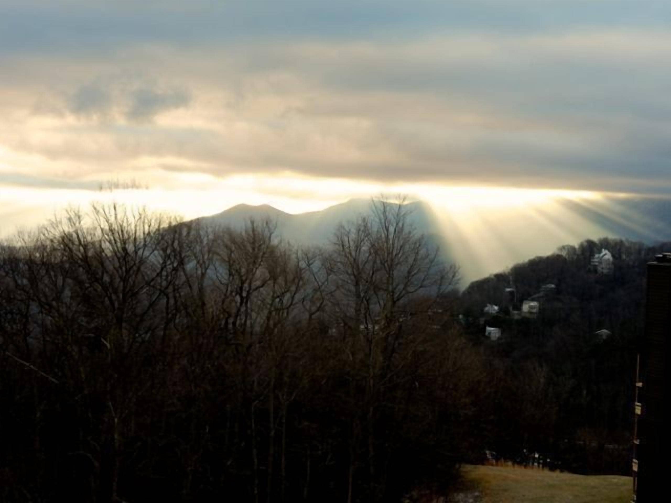 A mountainous landscape with a clear sky and sunlight filtering through the clouds.